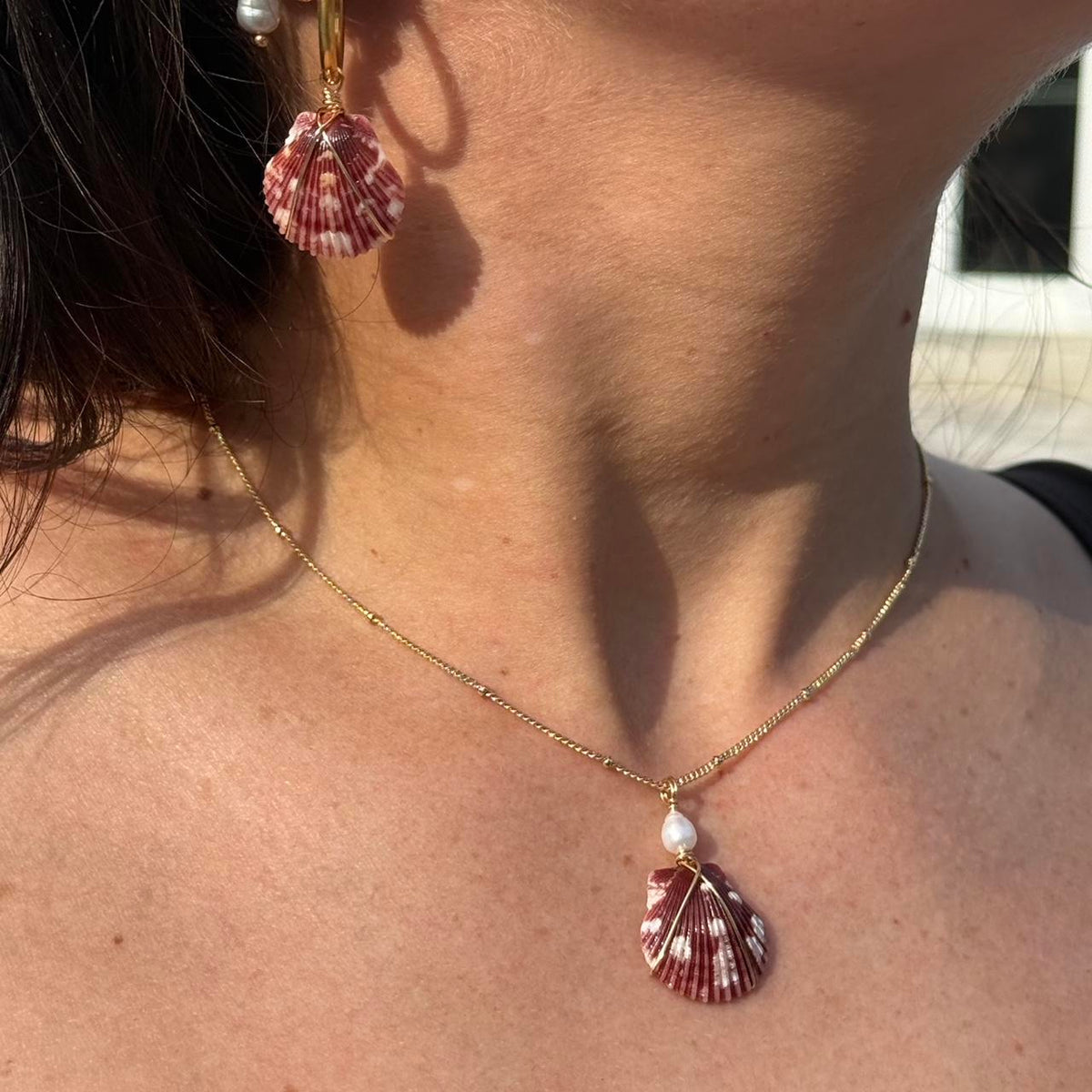 Burgundy scallop shell necklace with freshwater pearl accent worn in sunlight