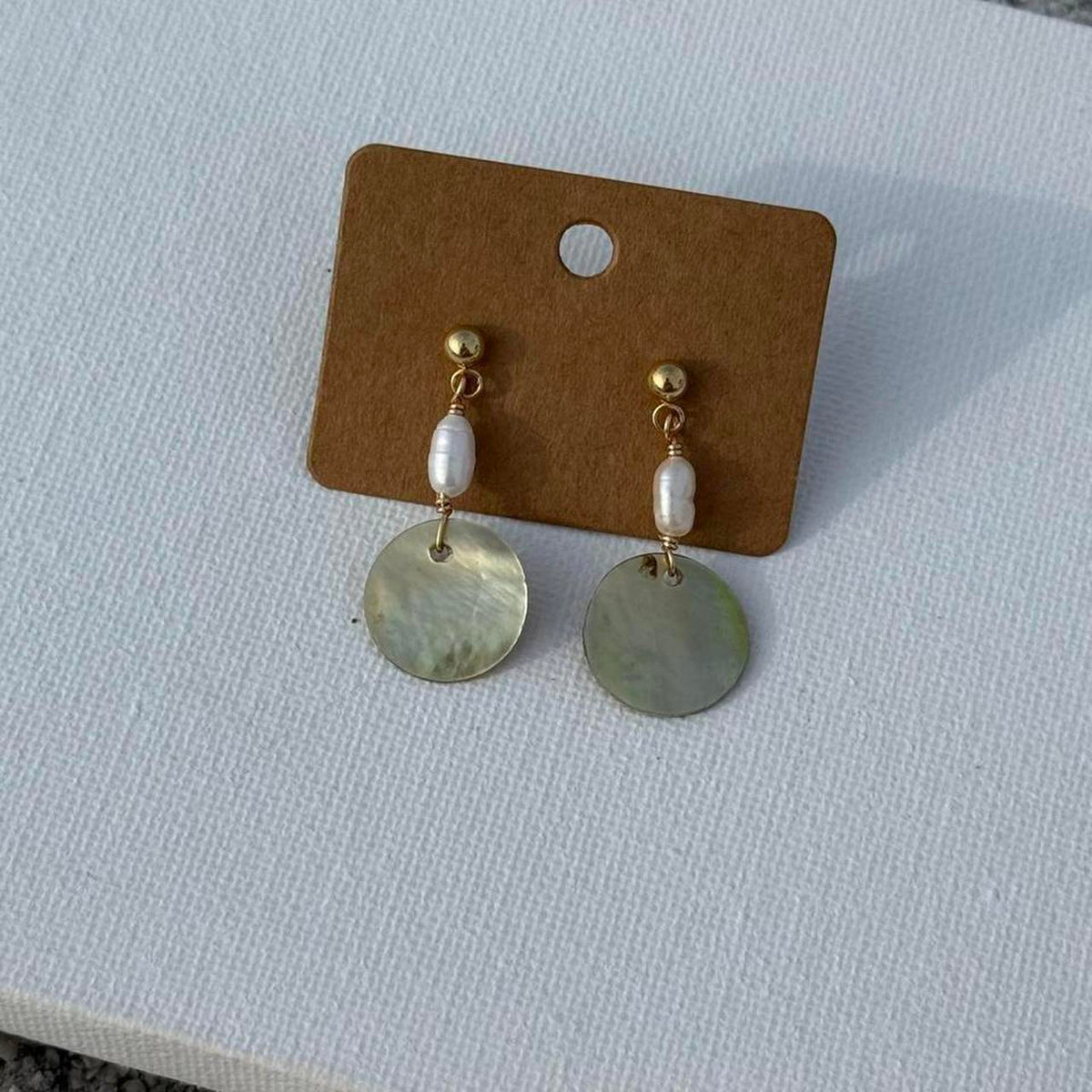 Gold Pearl Tide Earrings displayed on white fabric