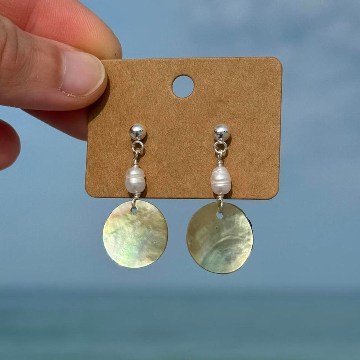 Silver Pearl Tide Earrings held against a coastal background