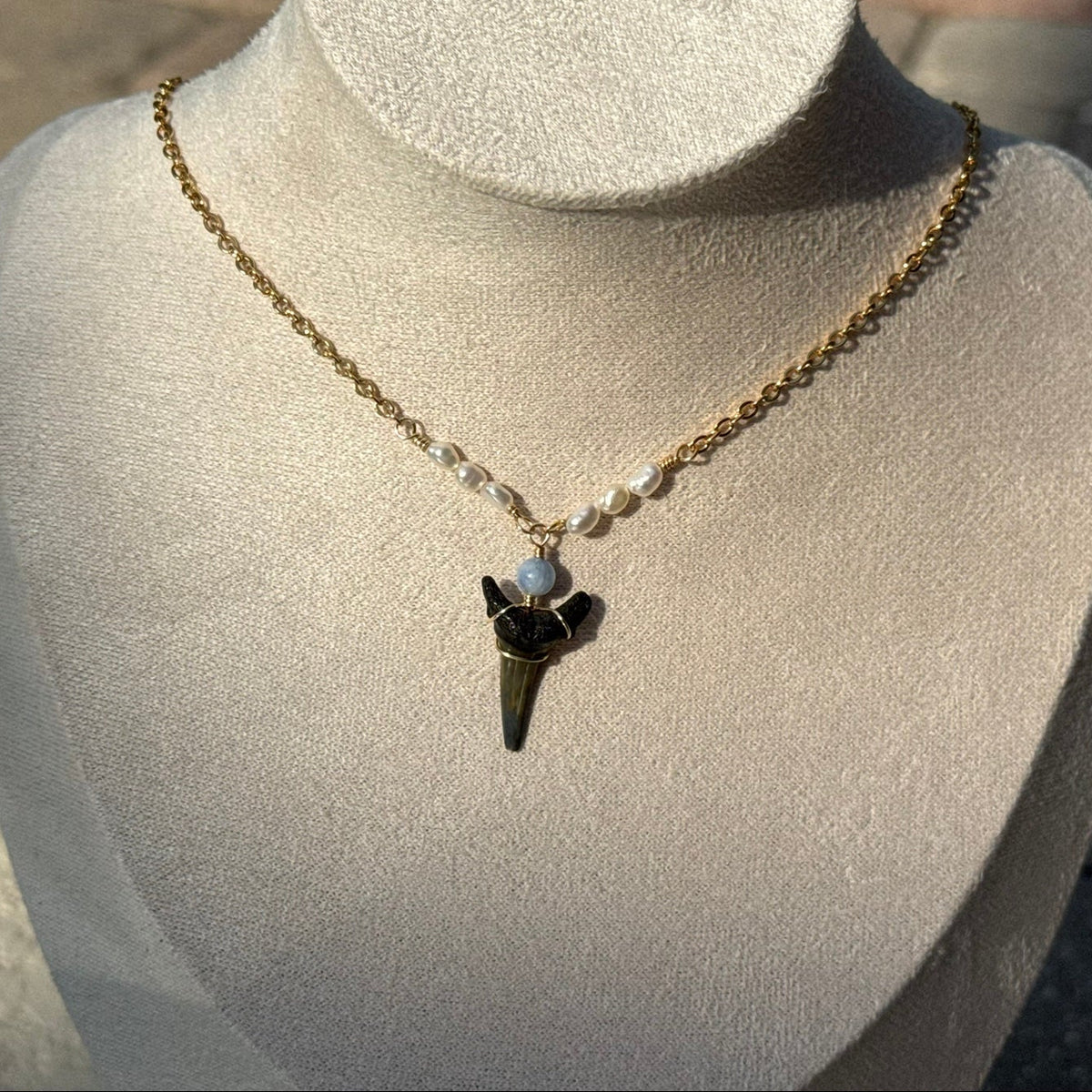 Close view of gold-tone shark tooth necklace with pearl details