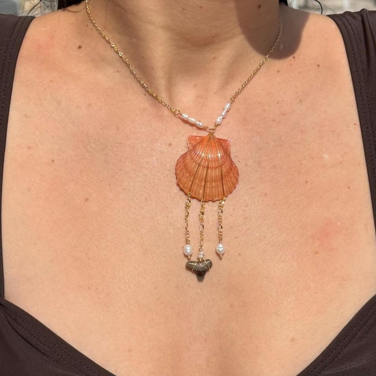 Close view of orange scallop shell necklace with pearl and shark tooth drops